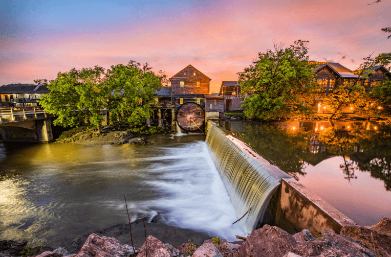 Small river with dam and waterfall with vegetation and buildings, with sunset sky in the background