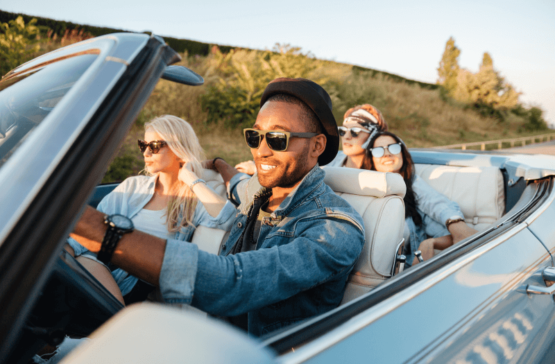 Group of friends joyfully riding together in a convertible car on a sunny day.