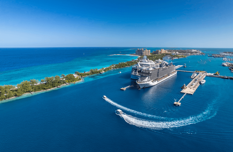 A cruise ship is docked in the ocean, adjacent to a luxurious resort, under a clear blue sky.