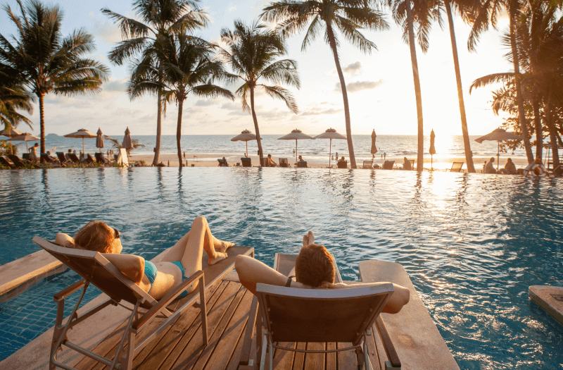 Two women sit comfortably in chairs by the pool, enjoying a moment of relaxation under the sun.