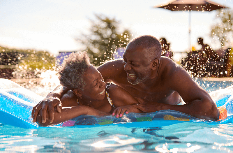 Older man and woman enjoying a sunny day in a swimming pool.