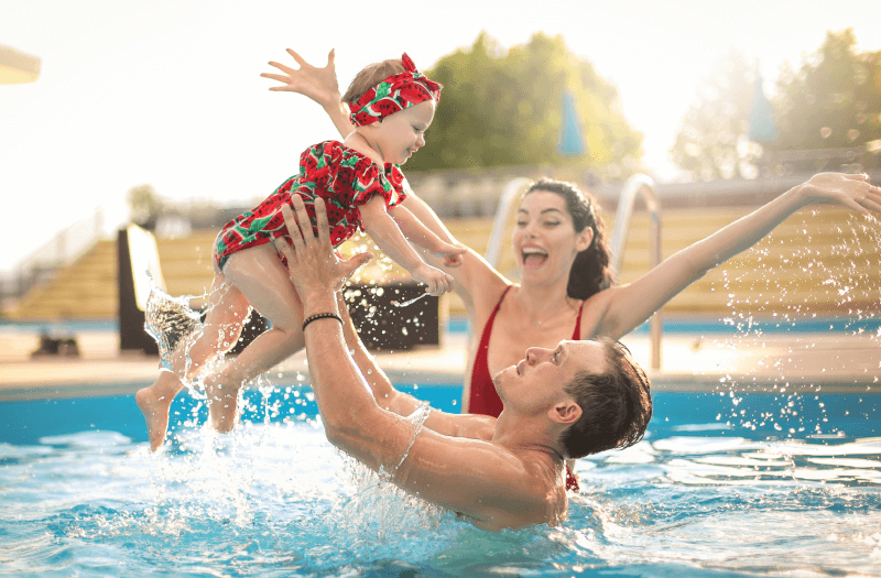 A man and woman joyfully hold a baby while enjoying a sunny day in a swimming pool.