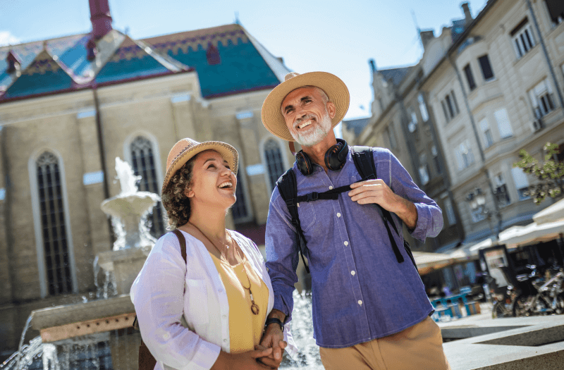 A senior couple strolls hand in hand through a bustling city, enjoying their time together amidst urban scenery.