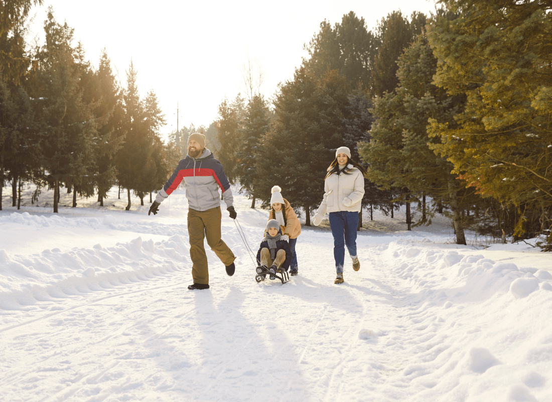 Man, woman, and two children walking on a snowy path surrounded by trees