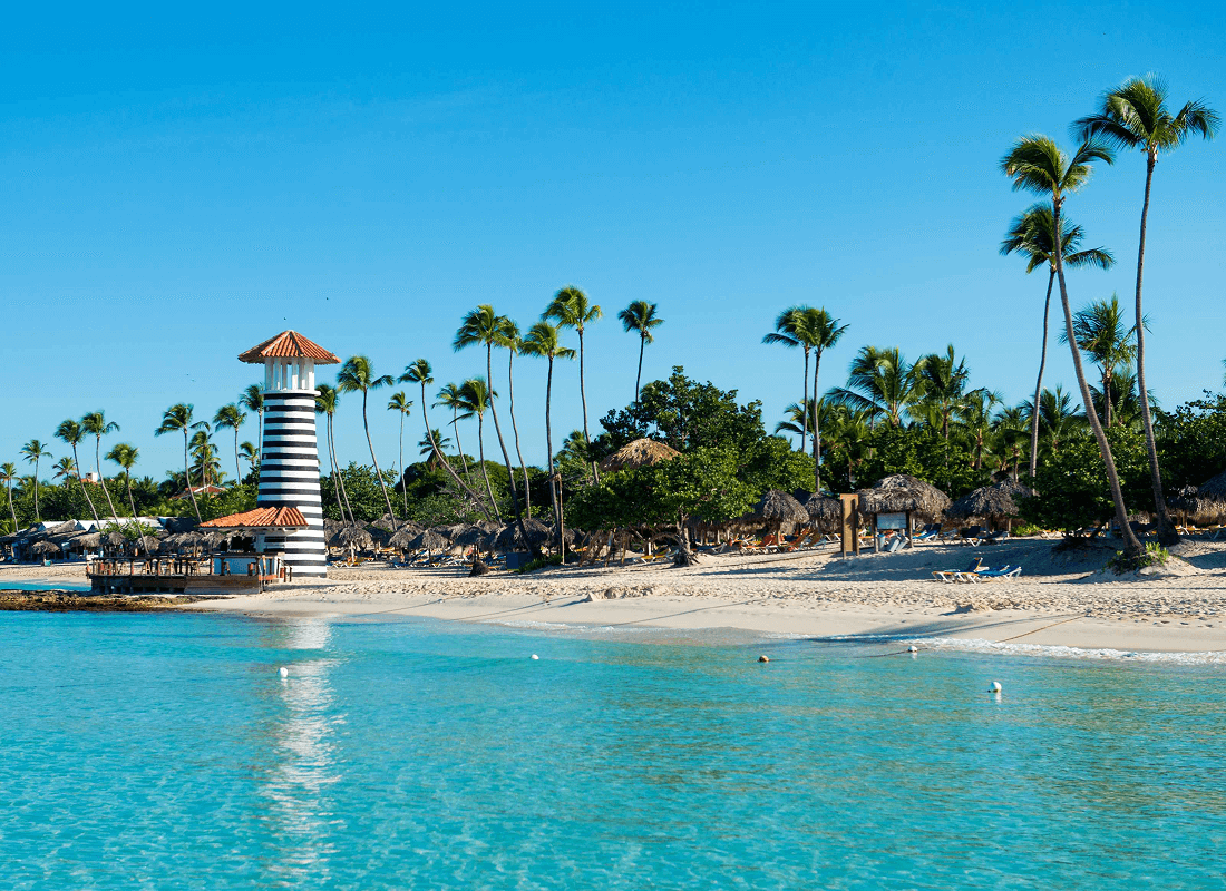 View of a beach with palm trees and a small lighthouse, with clear sky in the background