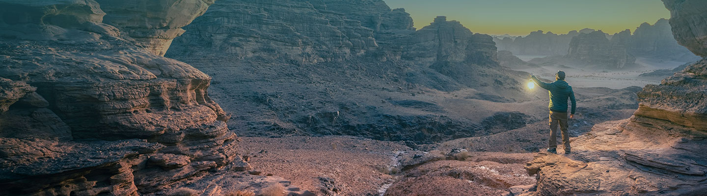 Person hiking though a canyon in the evening carrying a lantern