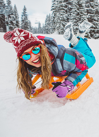 Person smiling on a sled in the snow, with snowy trees in the background