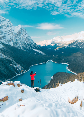 Person standing in snow with lake and snowy mountains in background