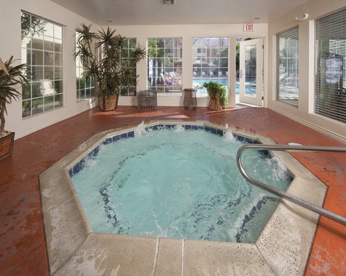 An indoor swimming pool with hottub and chaise lounge chairs.